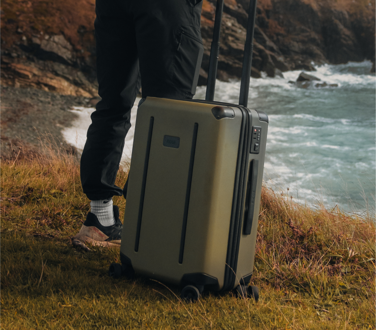man holding a ridge matte olive carry-on looking at the sea