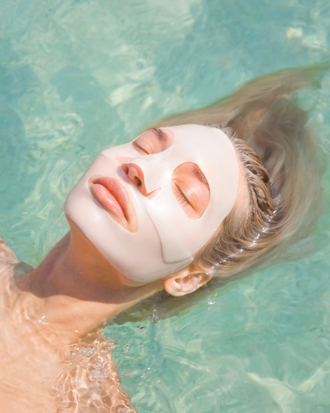 Woman relaxing in water with a facial mask.