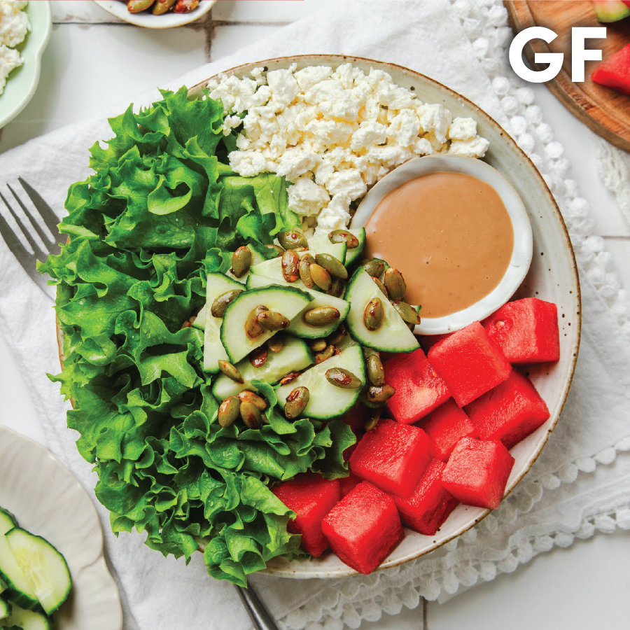 A colorful salad with lettuce, watermelon, cucumbers, and a dip on a plate.