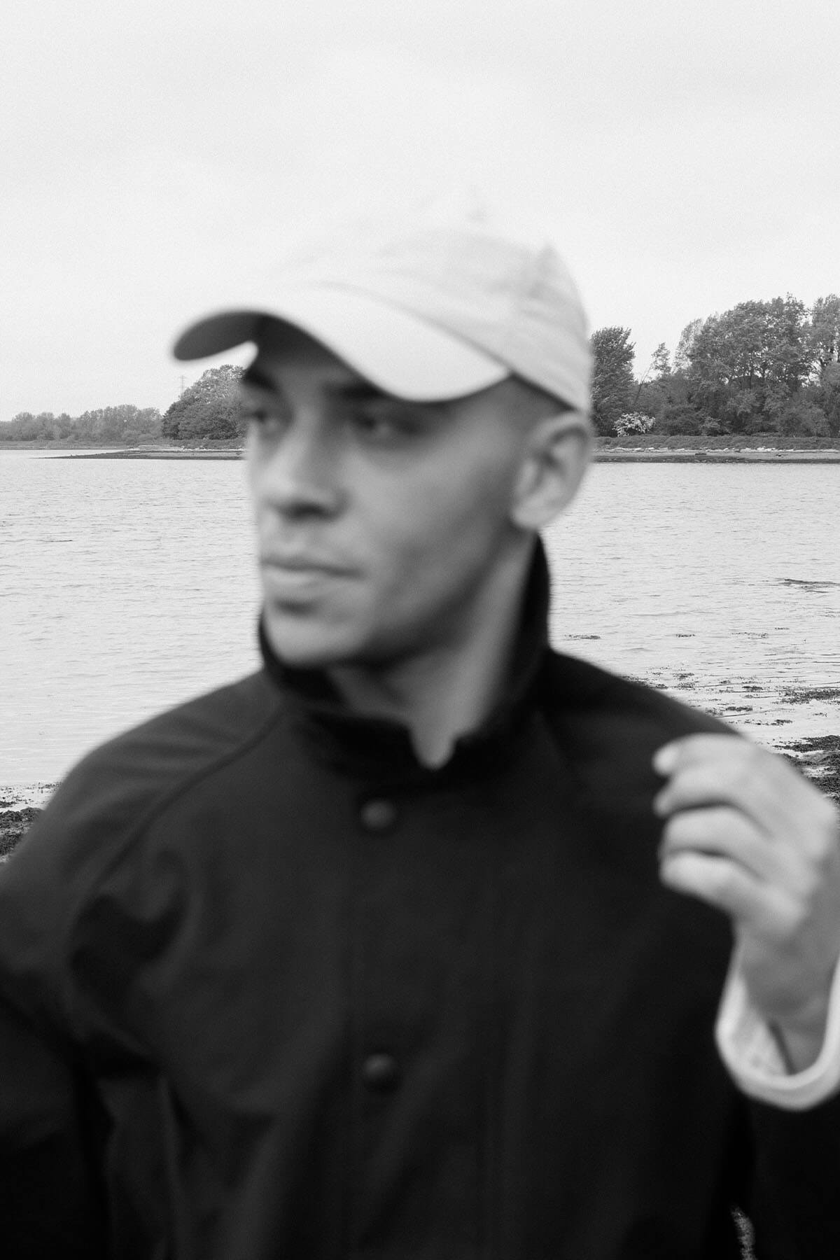 A man in a cap stands by a body of water.