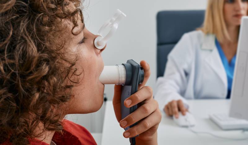 Child at the doctor’s doing a lung function test for asthma. They’re wearing a nose clip and blowing into a tube