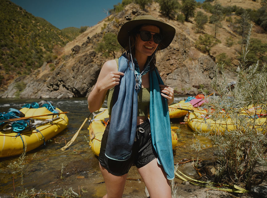 Person wearing a hat and towel near yellow rafts by a river.