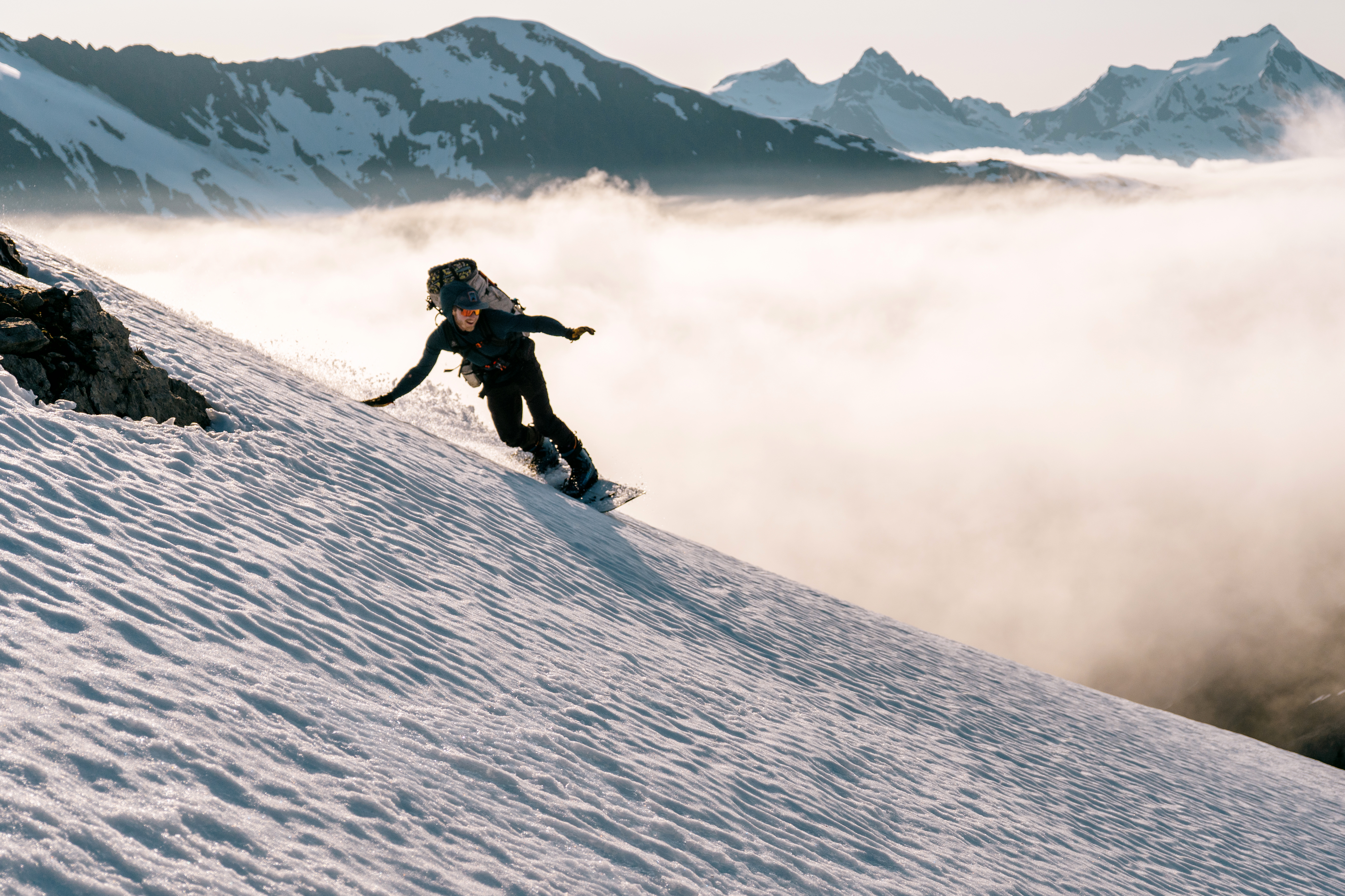 A snowboarder navigating a snowy slope with mountains in the background.