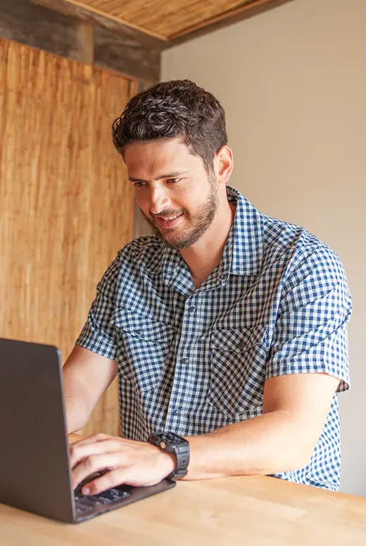 Man working on a laptop at a wooden table in a cozy setting.