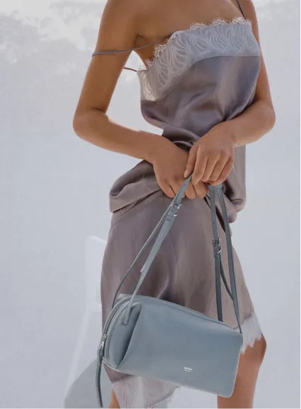 A person holding a blue handbag while wearing a silky dress.