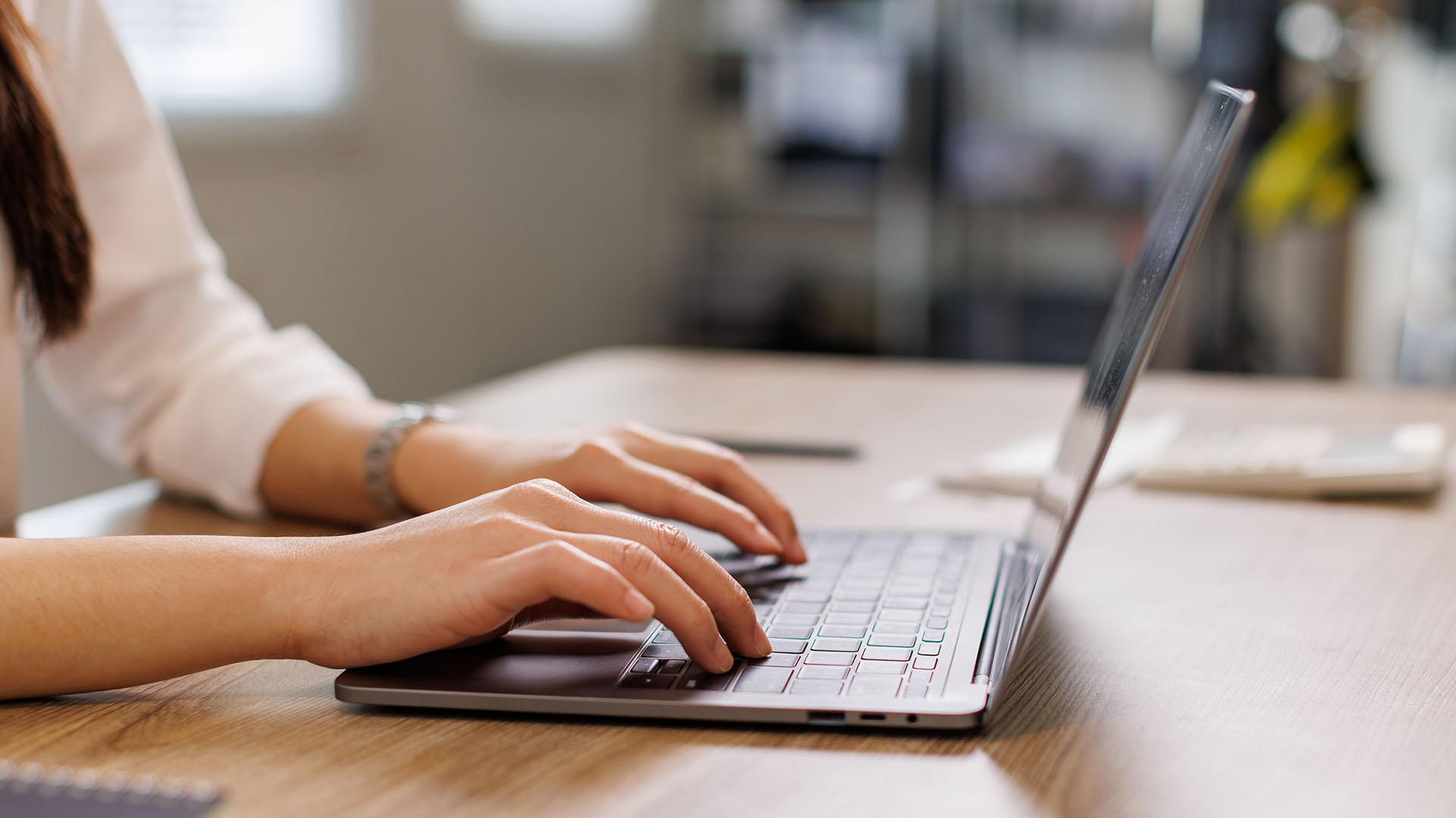 A picture of a person typing on a laptop at a wooden table
