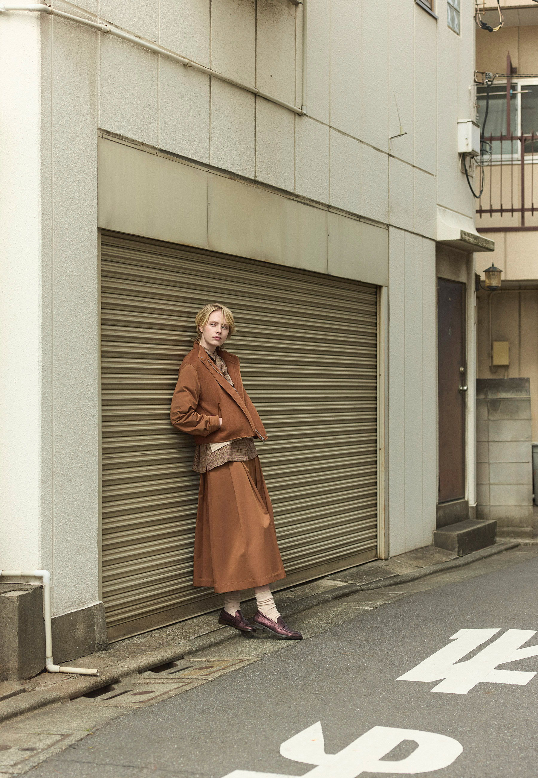Fashionable person in a brown outfit standing beside a closed garage door.