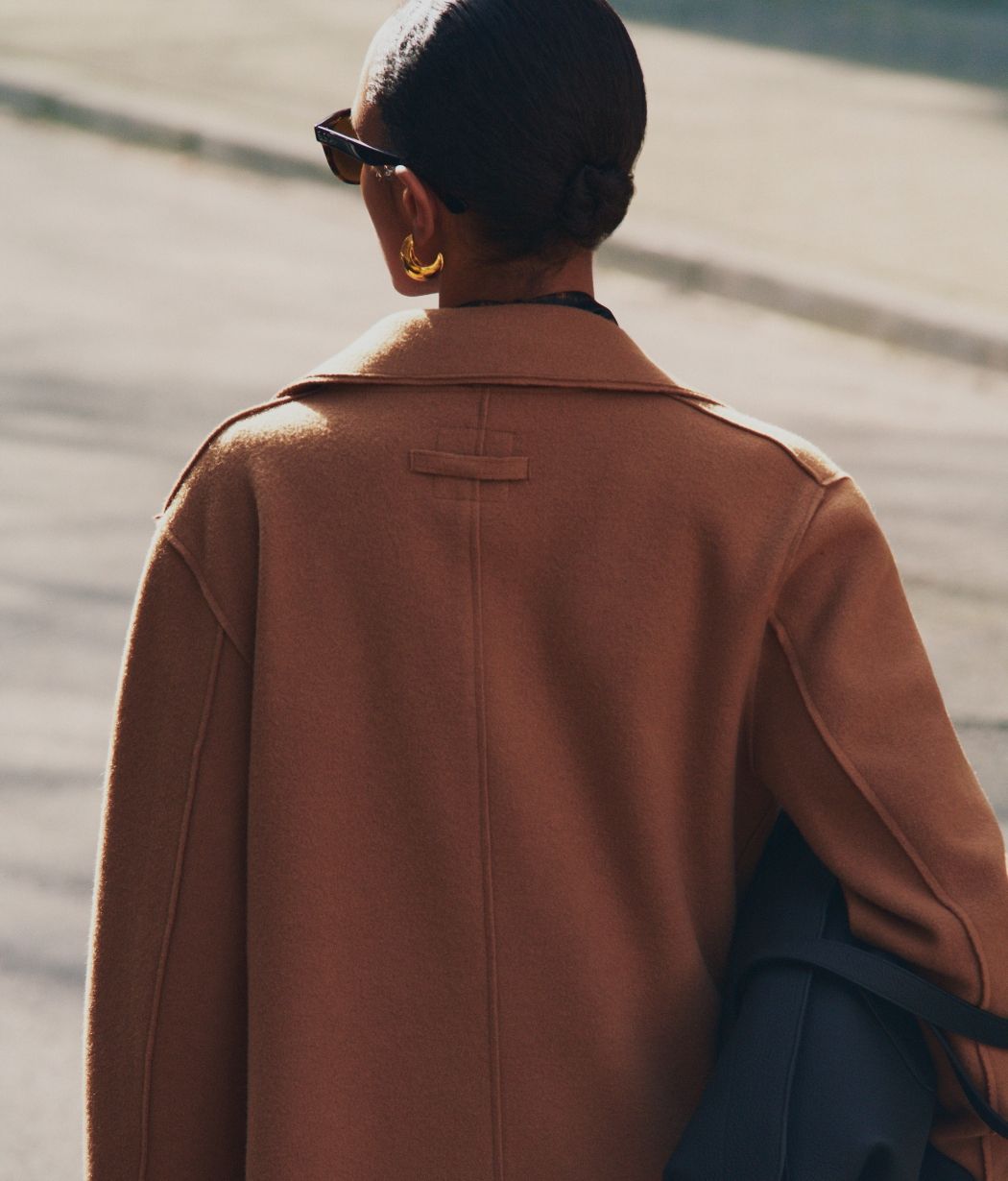 A person in a brown coat walking away.