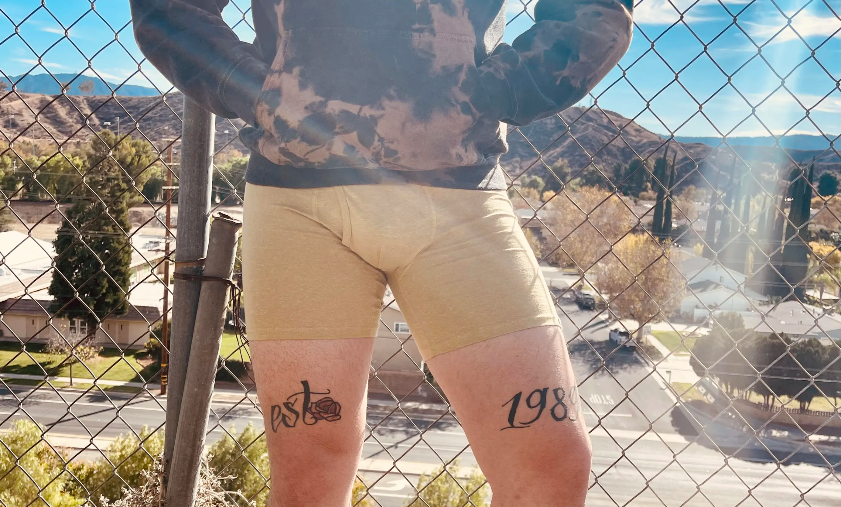 man in nude boxers leans against chain link fence