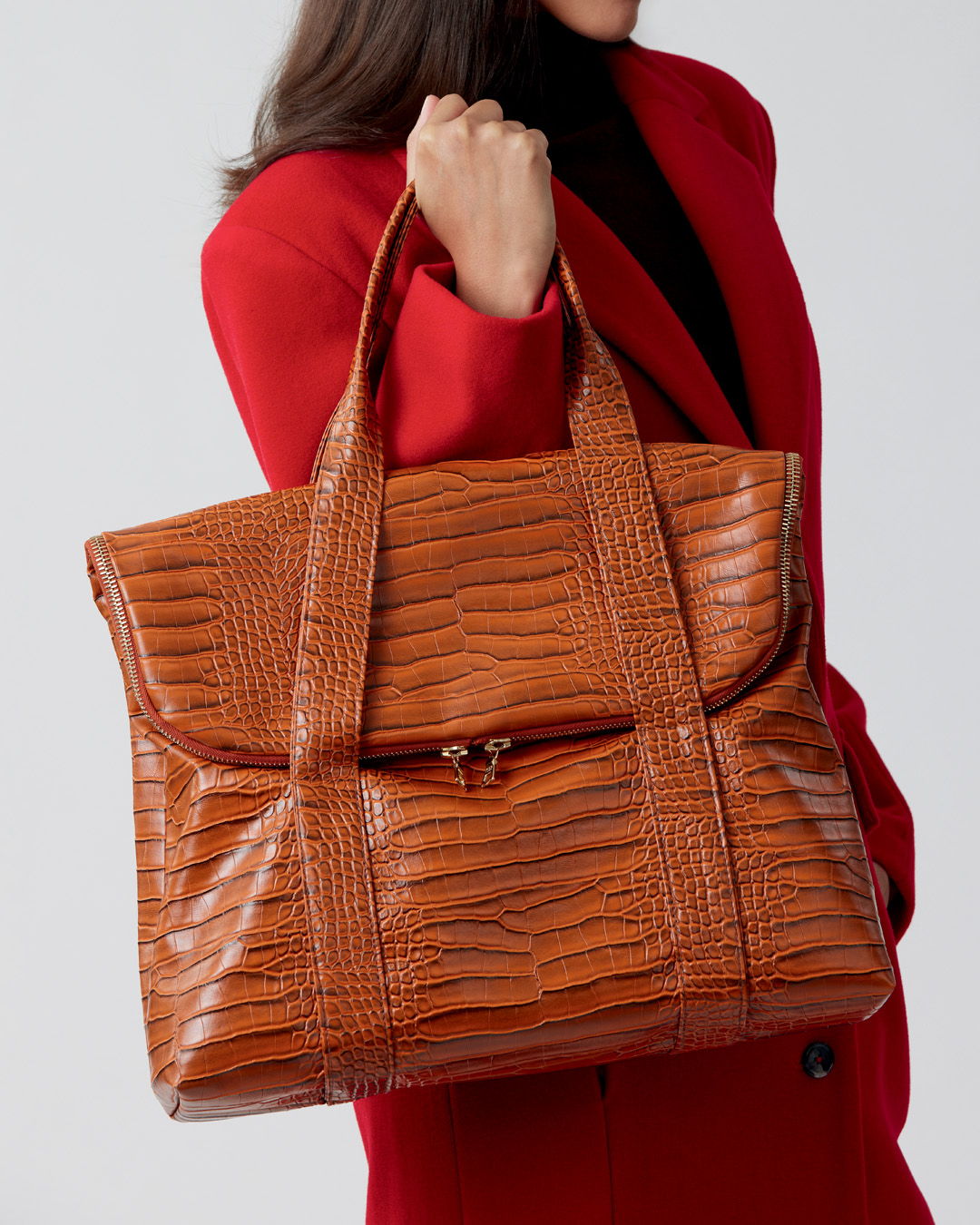 A woman in a red coat holding a large brown handbag.