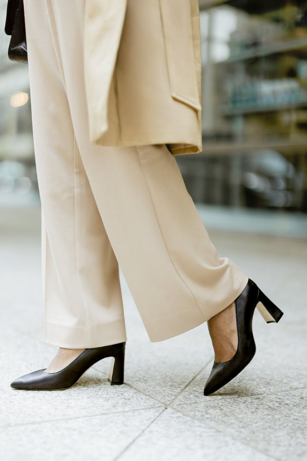 A person wearing beige pants and black high heels walking on pavement.