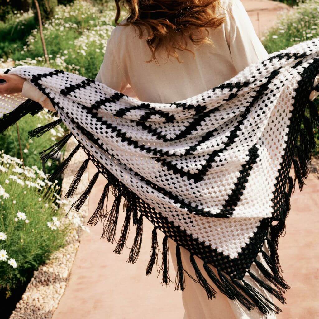 Person holding a black and white crocheted shawl in a floral setting.