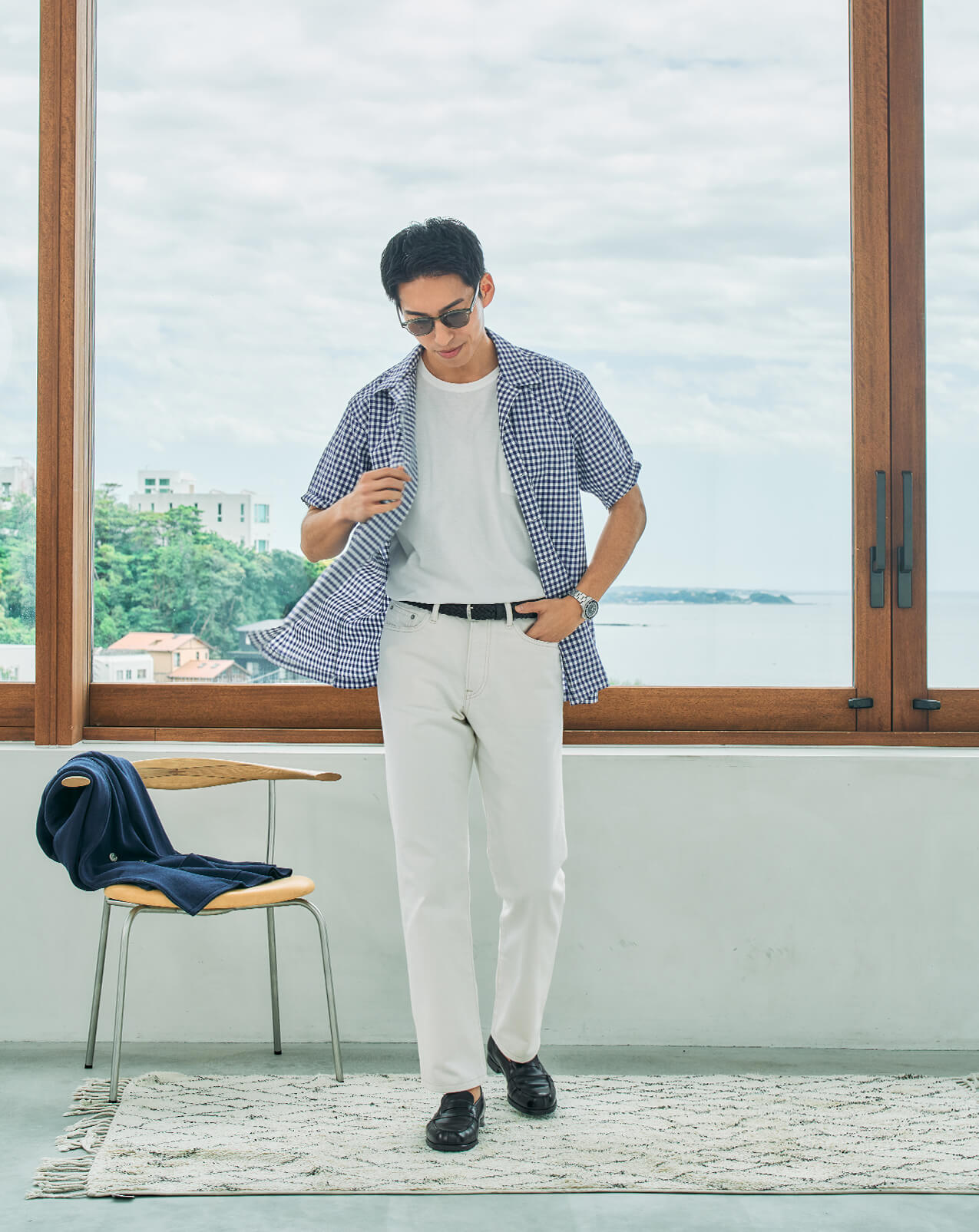 Person wearing a checkered shirt and pants, standing by a window.