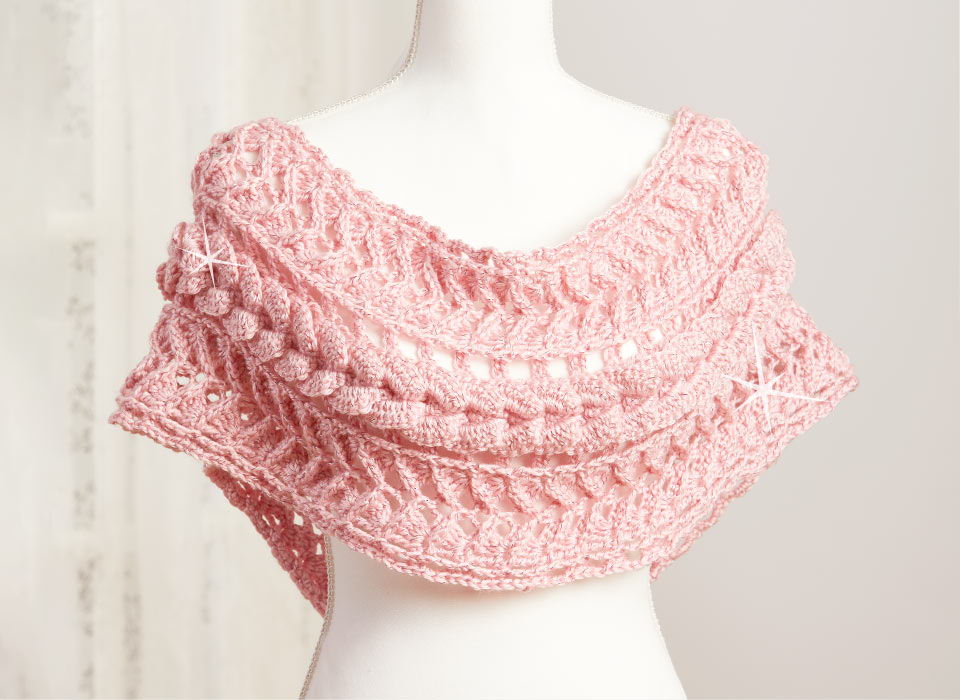 A sparkly pink crocheted shawl displayed on a mannequin.
