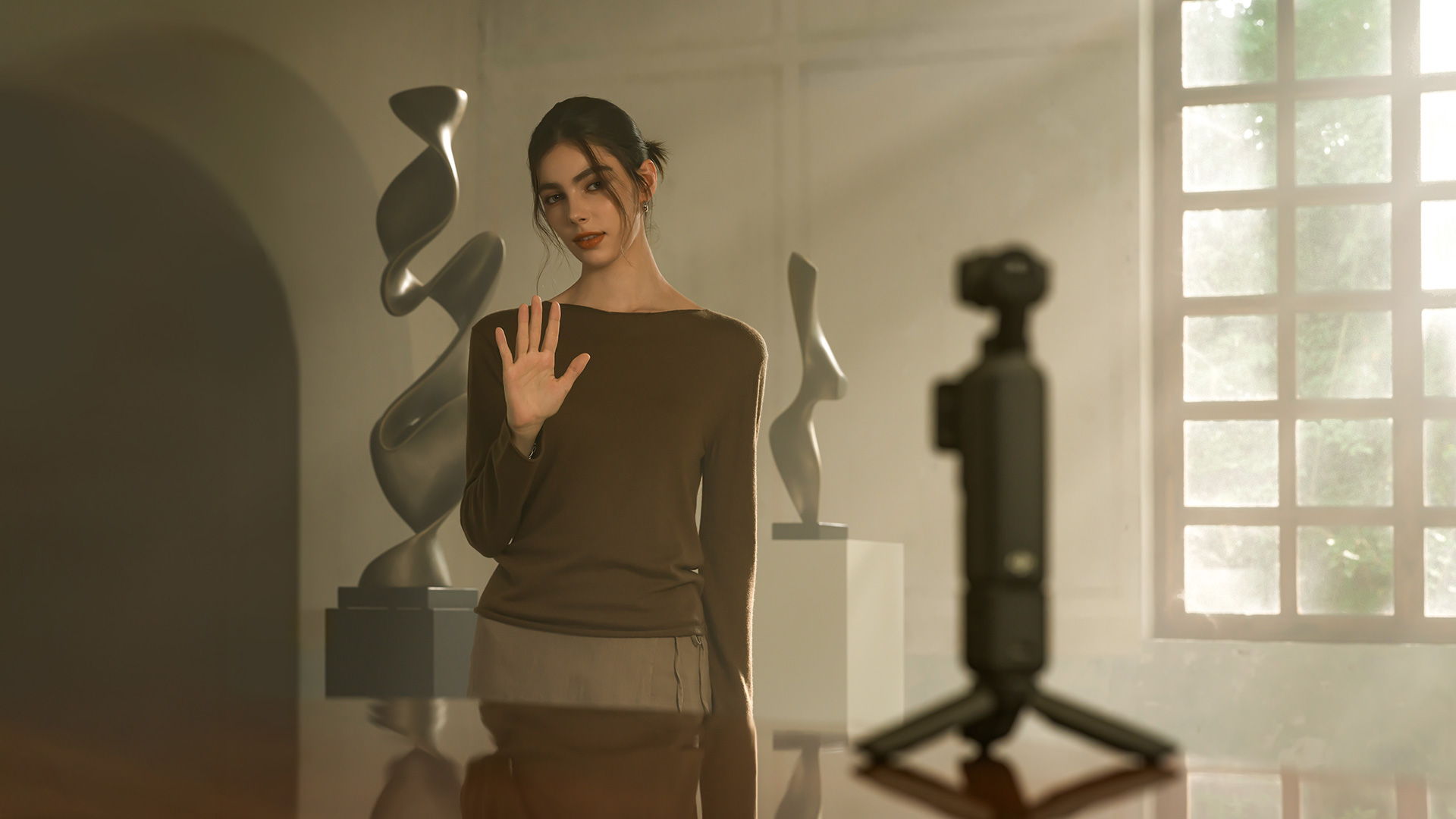 A woman uses gesture control to record on the DJI Osmo Pocket 4 in a modern art gallery.