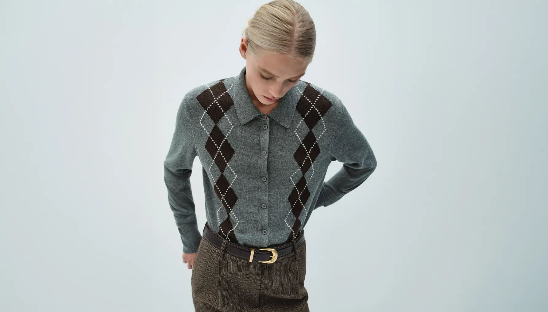 Person wearing a patterned sweater and brown pants, looking down against a light background.