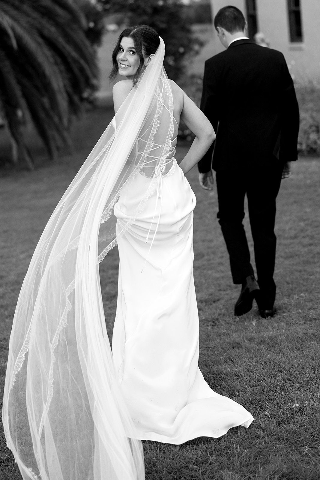 Bride in a wedding dress with a long veil, groom walking away.