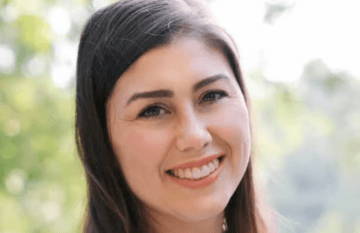 Smiling young woman with long hair outdoors in soft natural light.