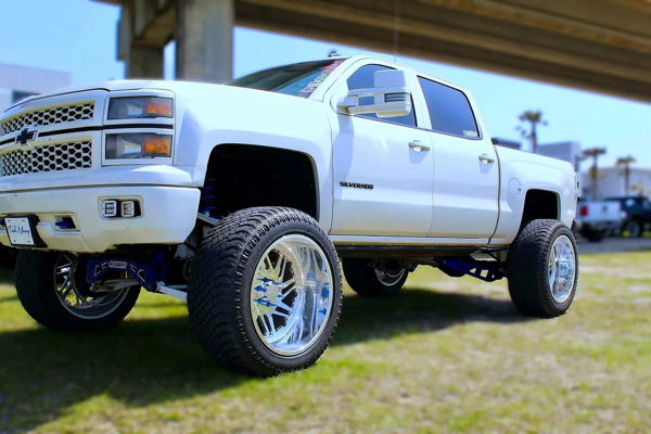 Low angle white lifted 2014 Chevrolet Silverado 1500 with chrome wheels and blue suspension at truck show Ethan's HornBlasters Outlaw train horn install photo 1