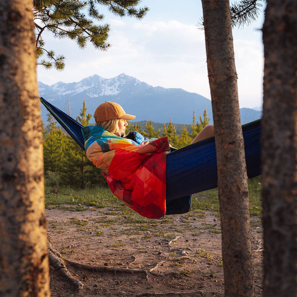 A young woman lounging in a hammock, wrapped in a Rumpl blanket, enjoying the outdoors.