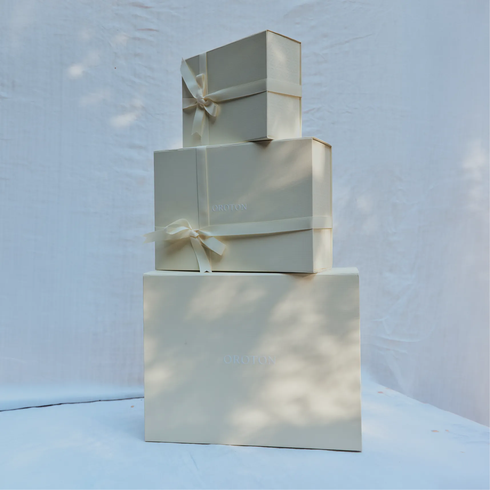 Three cream-colored gift boxes tied with ribbons on a light background.
