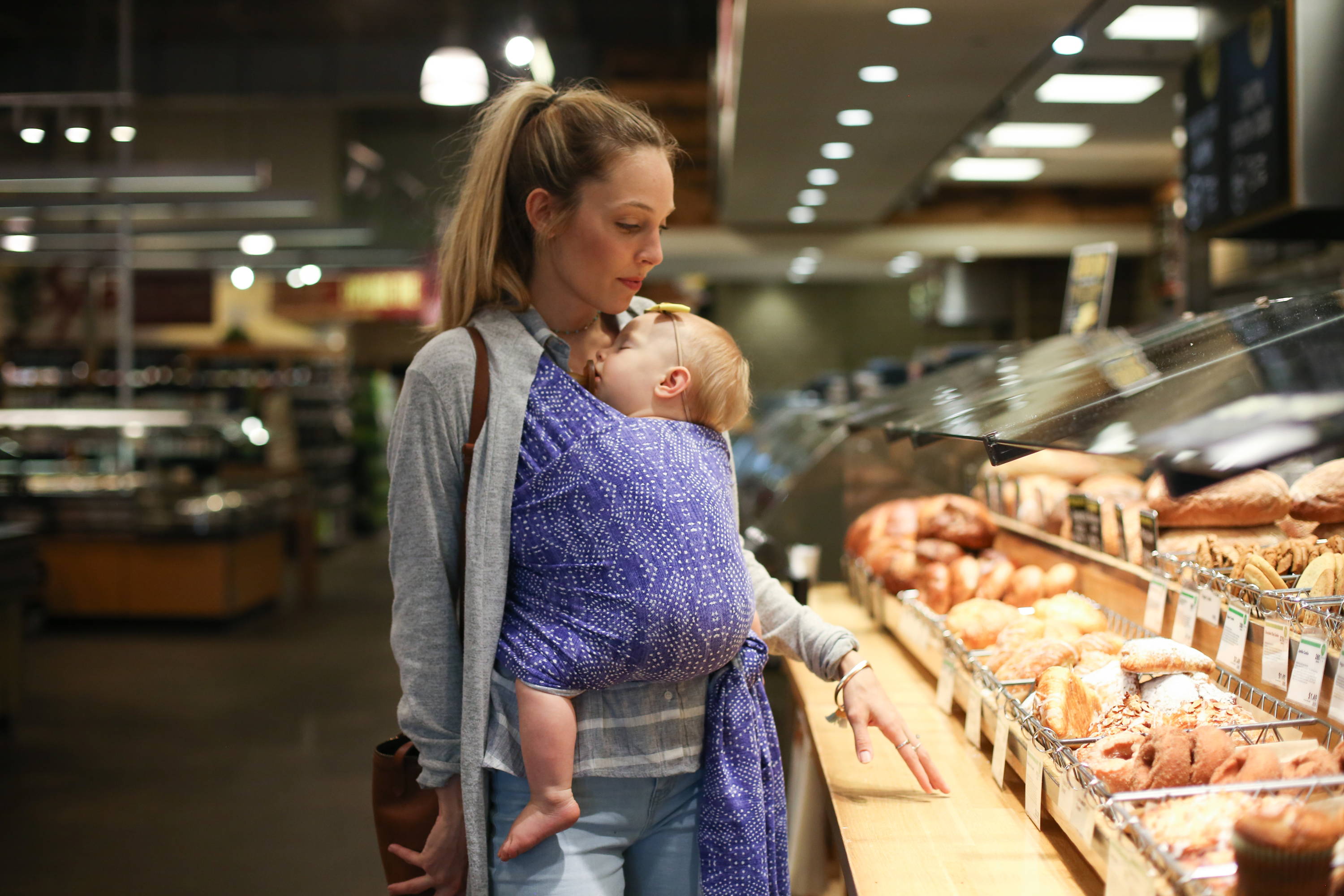 baby sleeping in soft cotton baby wrap while mom is shopping for groceries