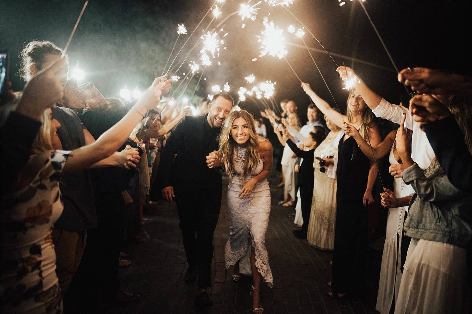 Newlyweds walking through guest sparkler arch at night