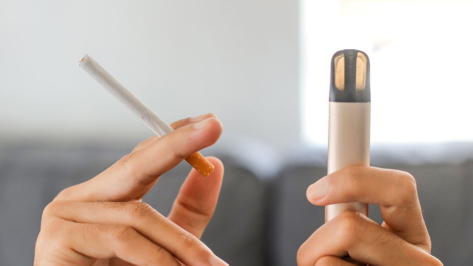A person holding a cigarette and a vaping device.