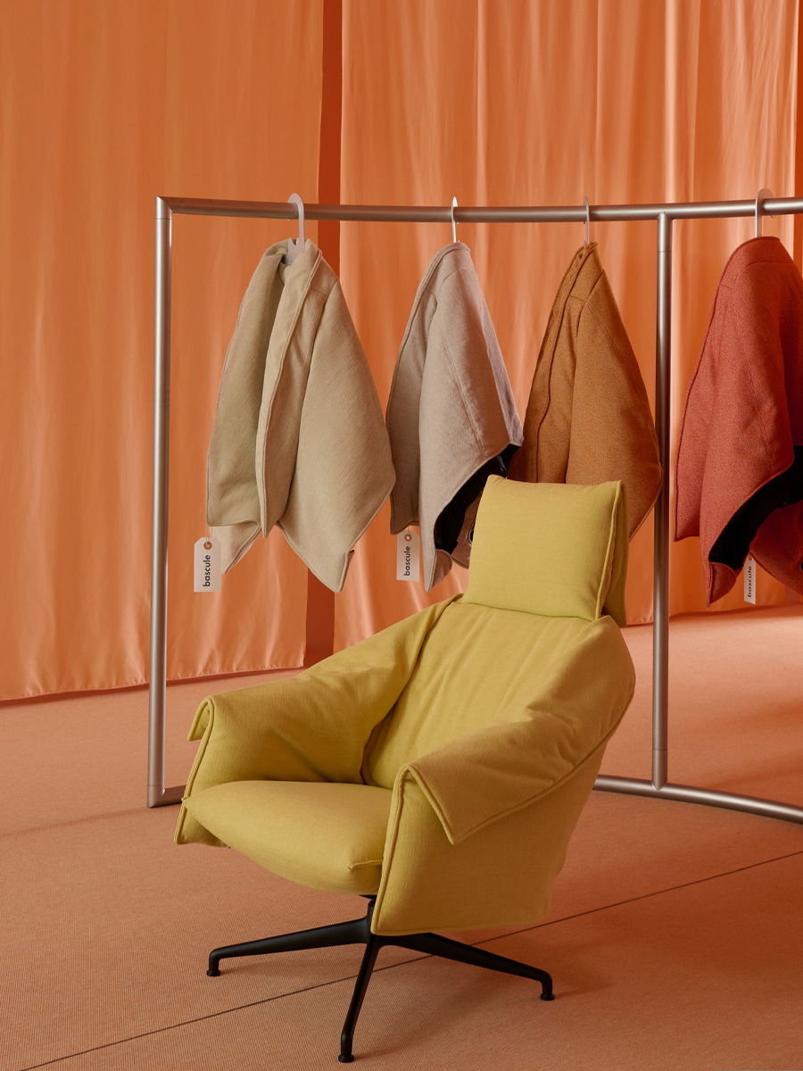 A yellow chair beside hanging coats in a softly colored interior.