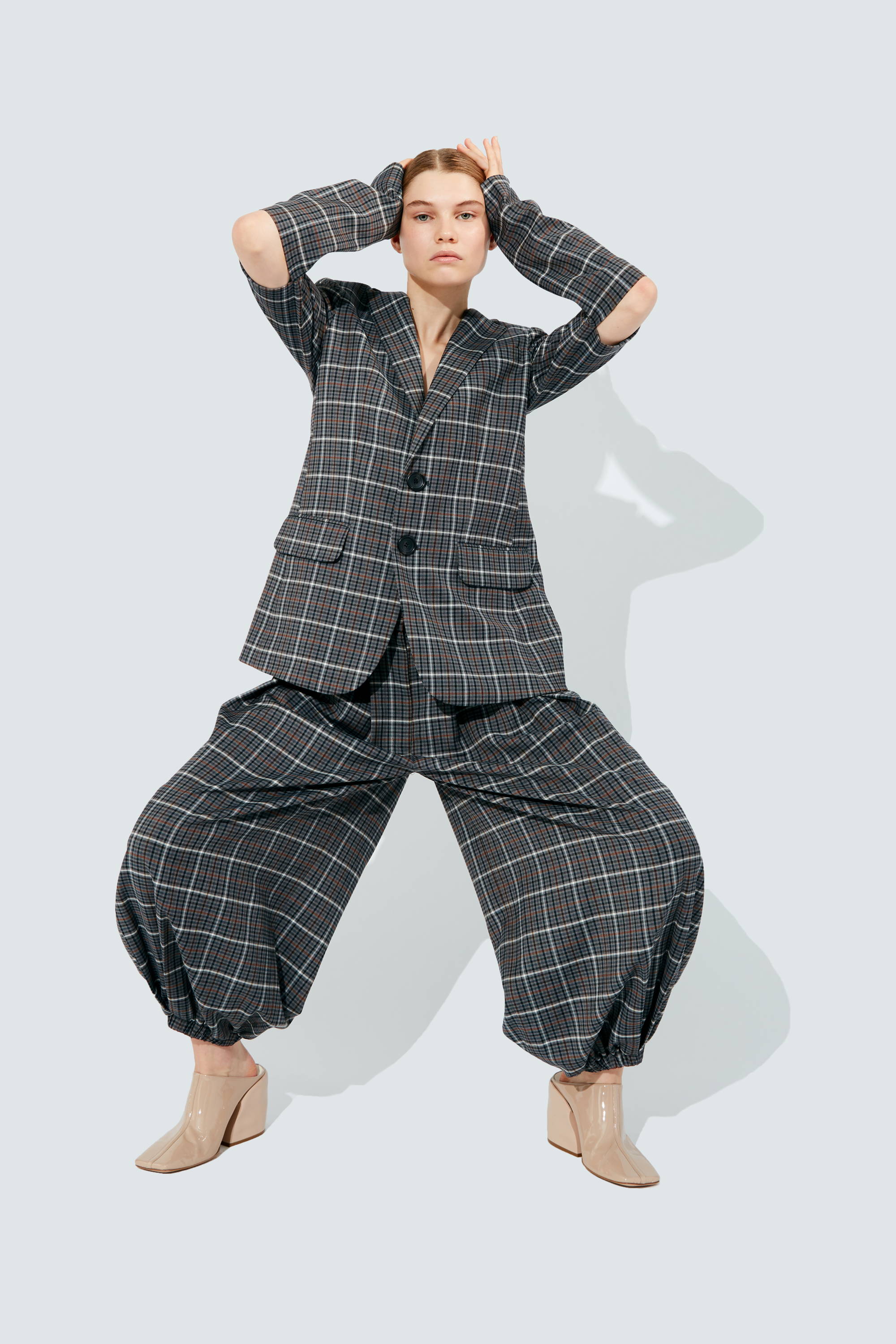 A model poses in a checkered suit with unique cut-out sleeves and wide pants.