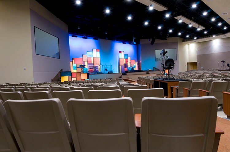 Empty auditorium with stage and colorful backdrop, lights on ceiling.