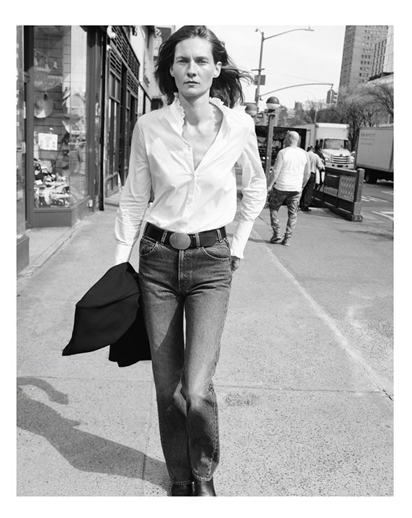 Person walking on a city street, wearing a white shirt and jeans.
