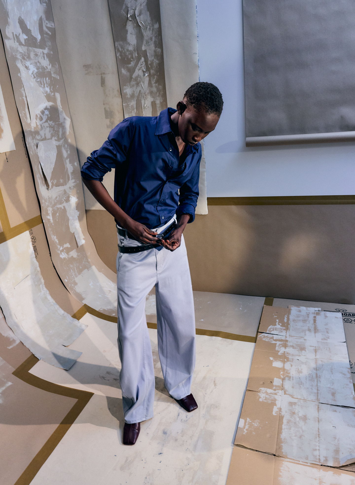 Person adjusting their belt while wearing a blue shirt and light trousers.