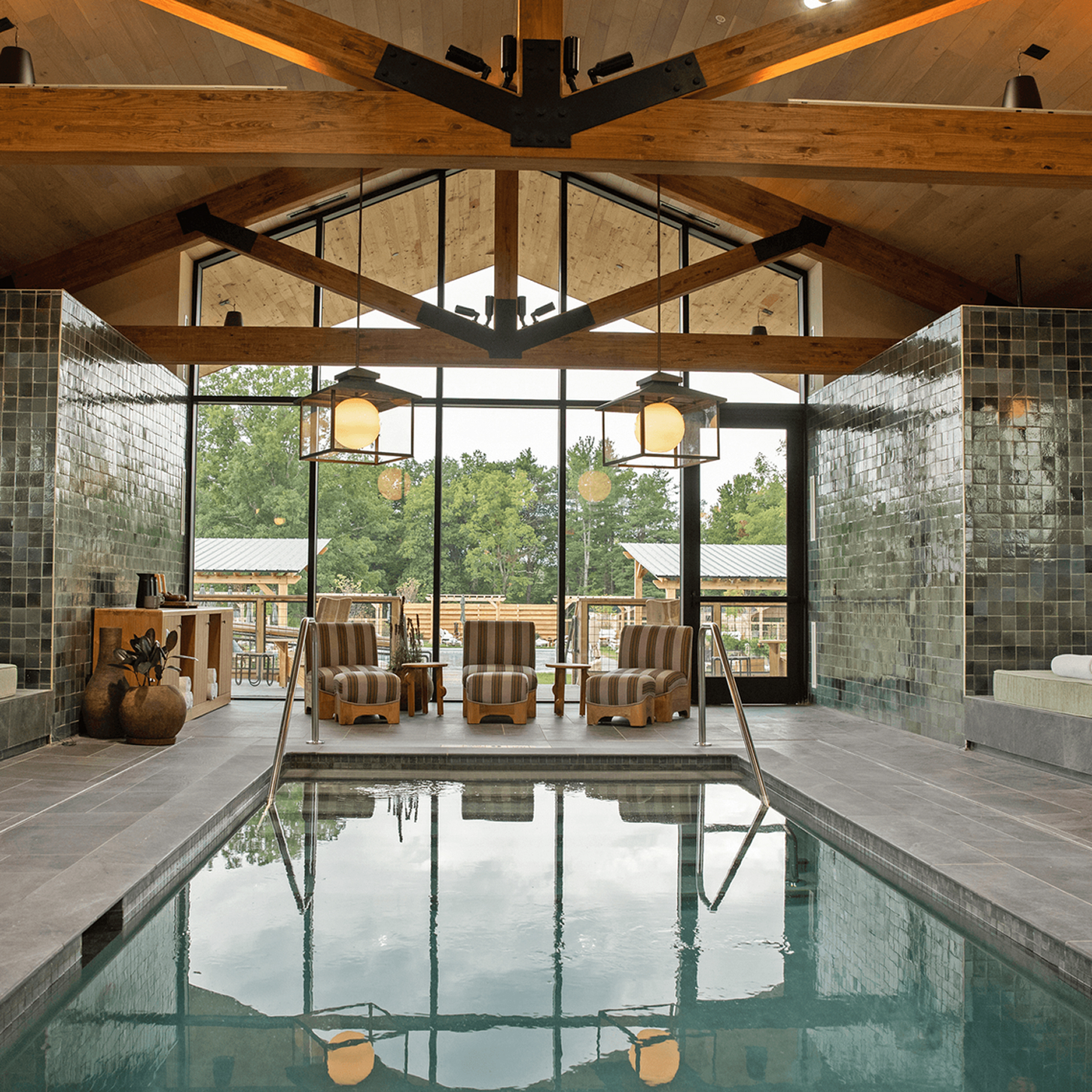 Indoor swimming pool with wooden beams and large windows overlooking greenery.