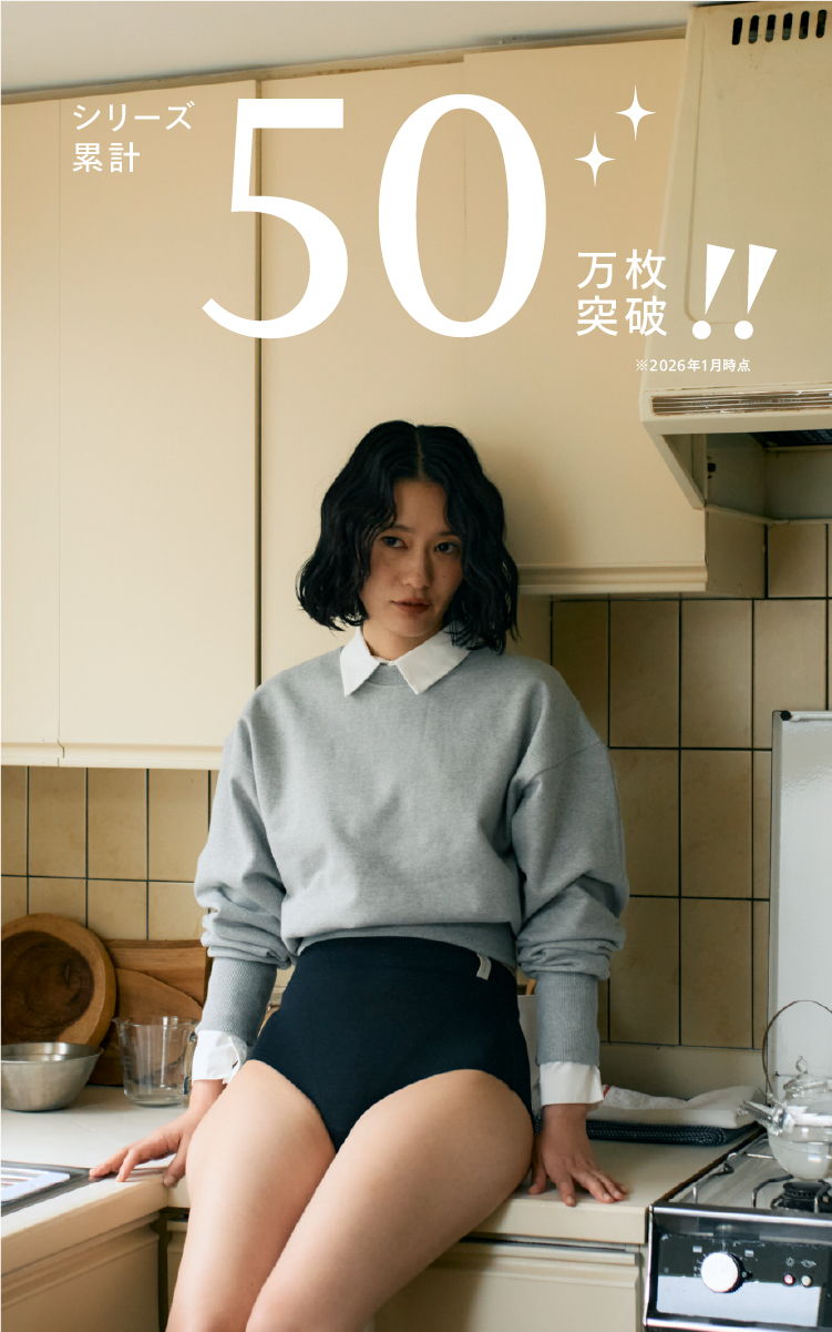 A person in a kitchen wearing a sweater and shorts.