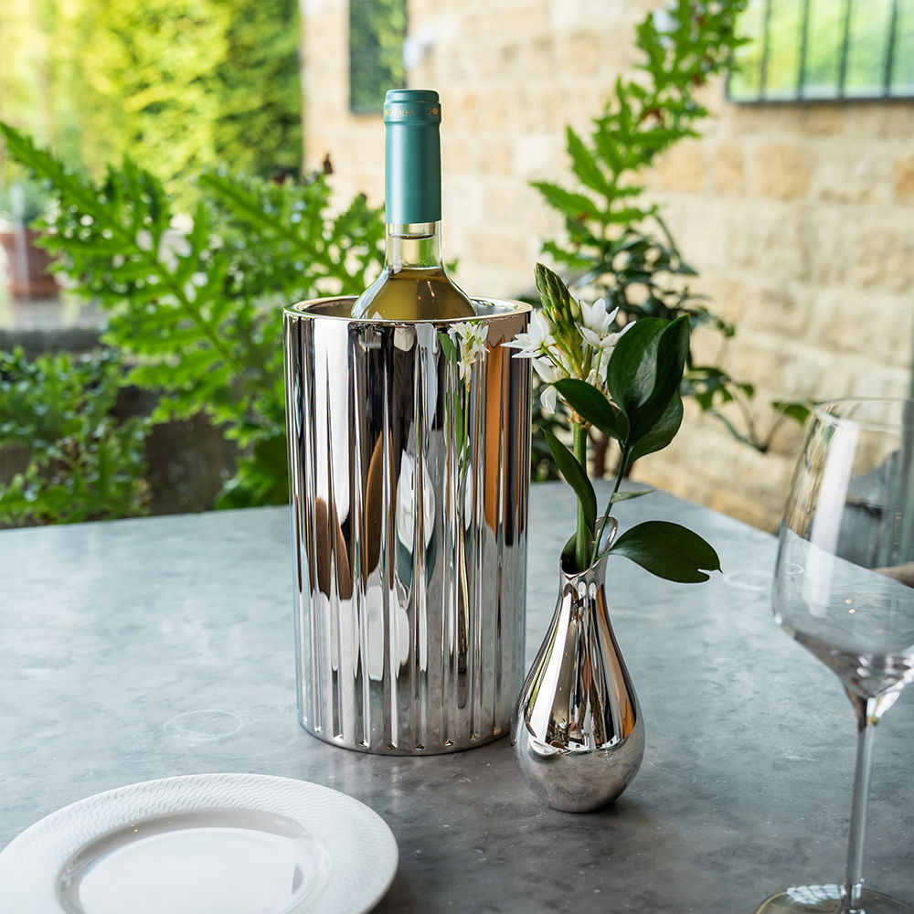A wine bottle in the Dorset Wine Cooler with flowers and glassware on a table.
