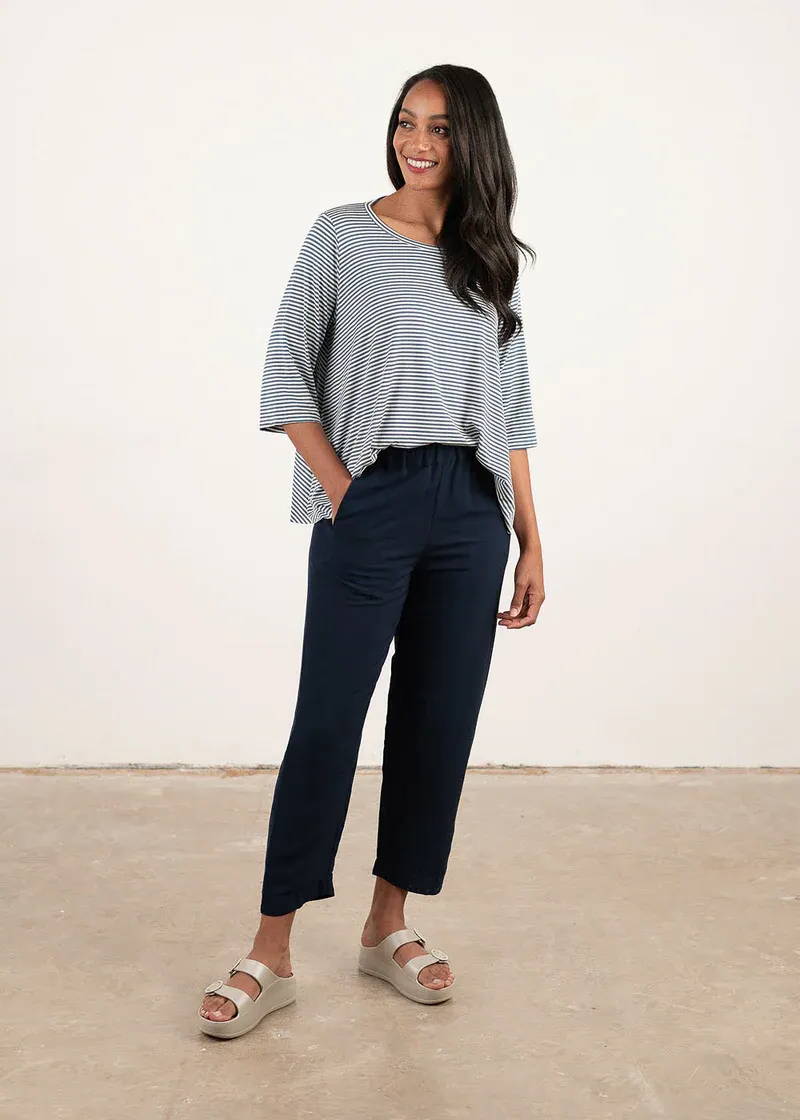A model wearing a loose, boxy blue and white striped t shirt with 3/4 sleeves, black trousers and off white chunky slides