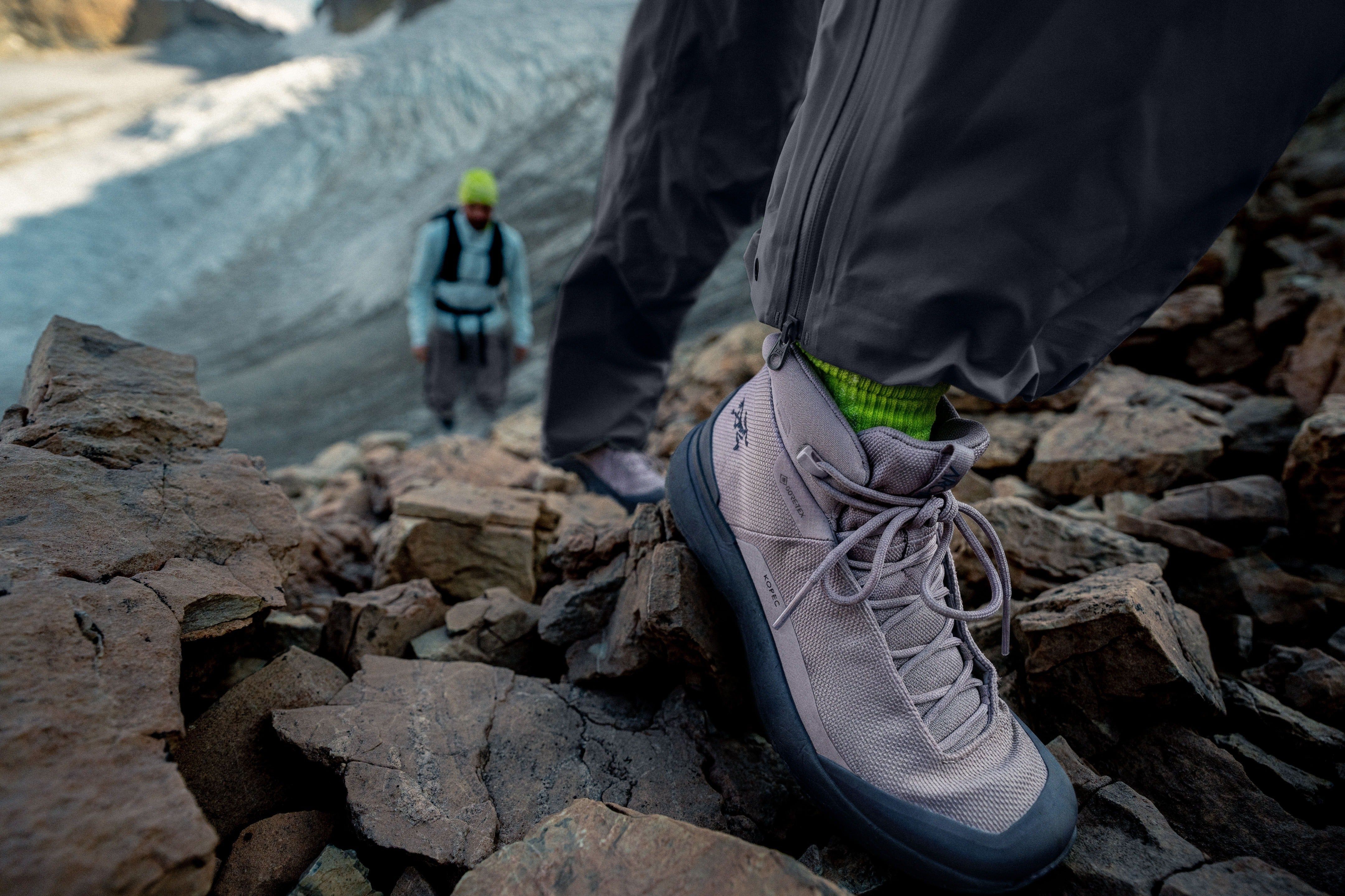 Hiker ascending rocky terrain wearing hiking boots, another climber in background.