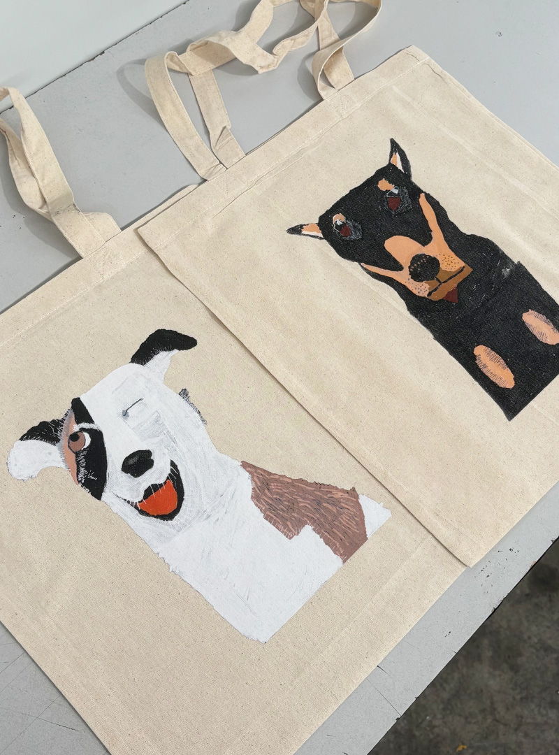 Canvas tote bags printed with illustrated dog portraits in a hand-drawn style.