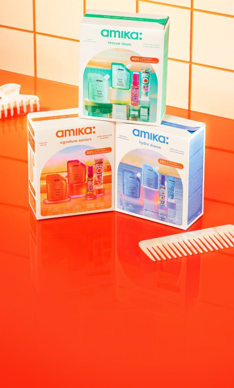 Three Amika hair care product boxes on a vibrant red surface.