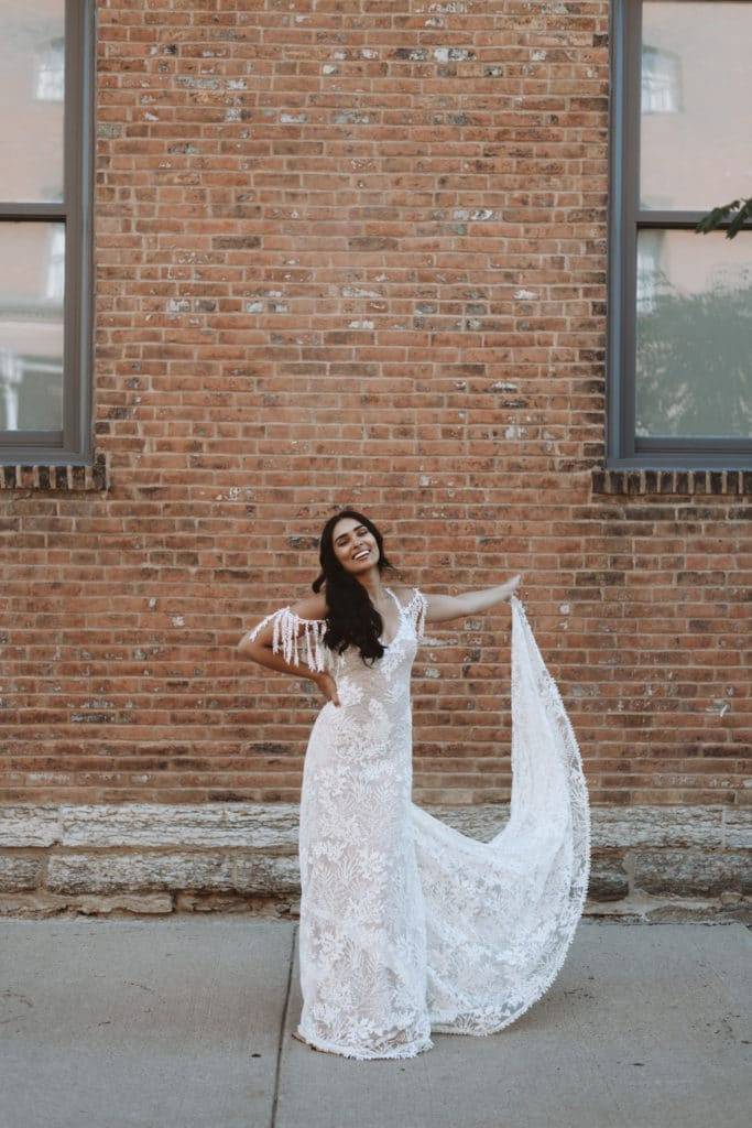 La novia lleva el vestido de novia Grace Loves Lace Sol contra un fondo de pared de ladrillo