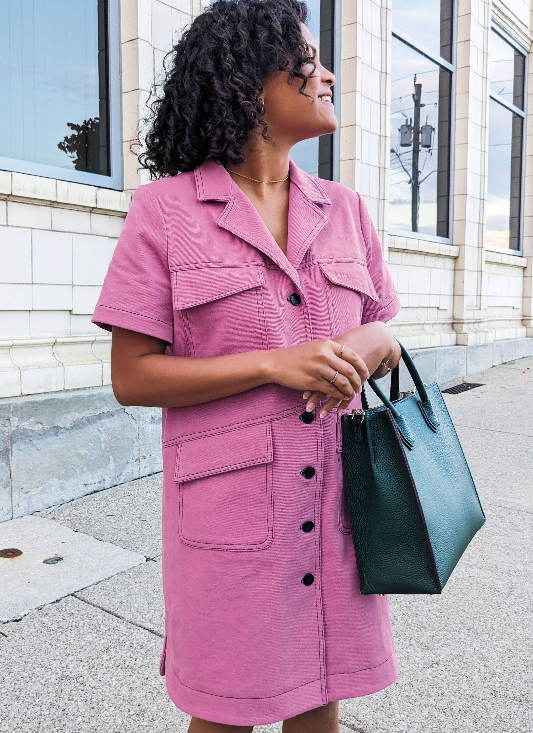 Woman with curly hair wearing a pink dress and black handbag