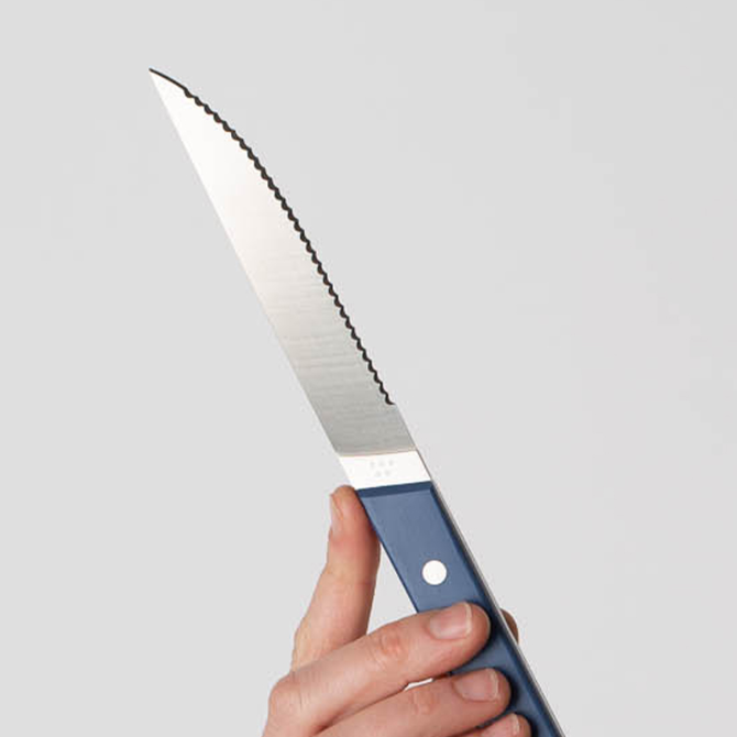 A hand holding a Blue Misen Steak Knife vertically with the blade’s tip facing upwards.