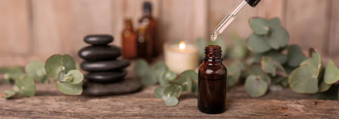 Brown glass bottle with dropper, stones, candle, and green leaves background.