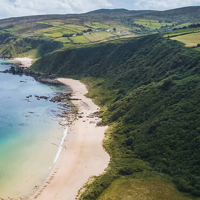an areal view of a coast with greens pushing up to the beach