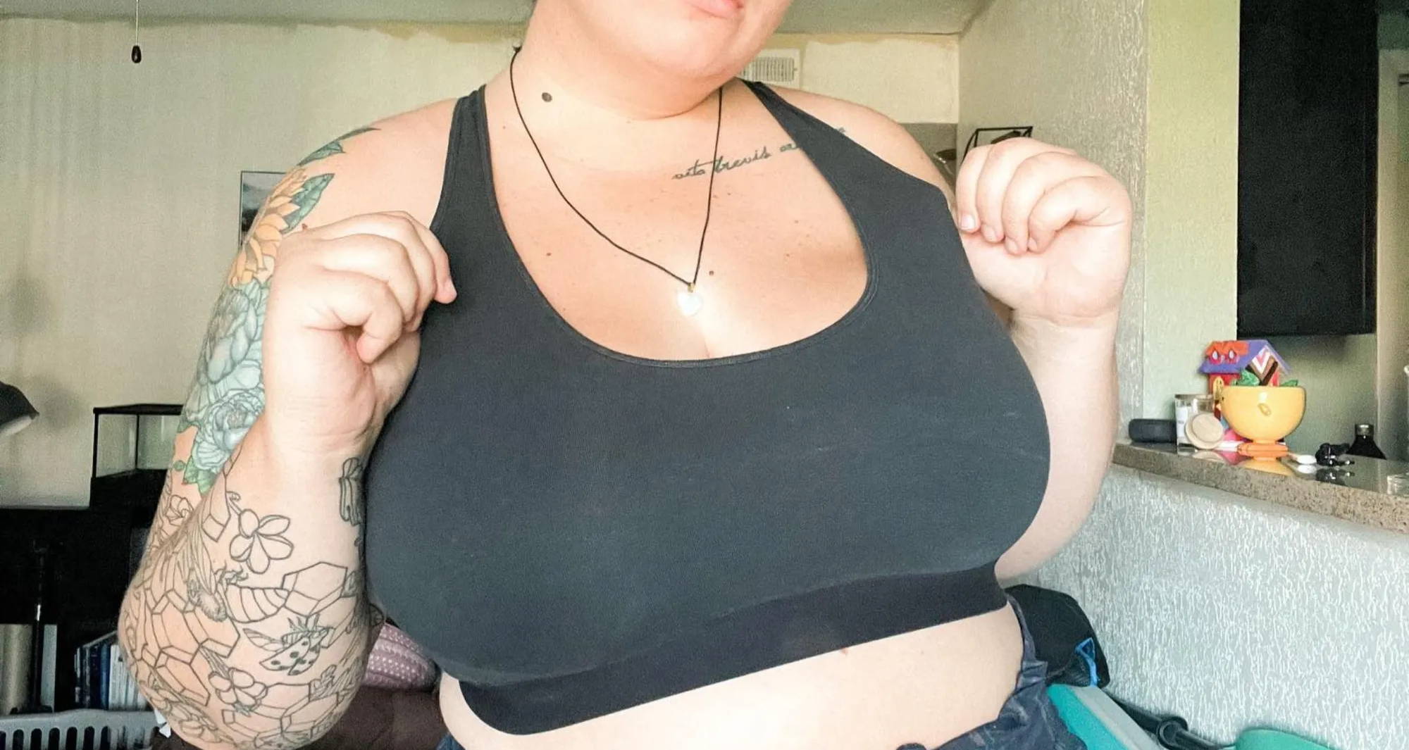 woman in black bralette and tattoos holds out her straps