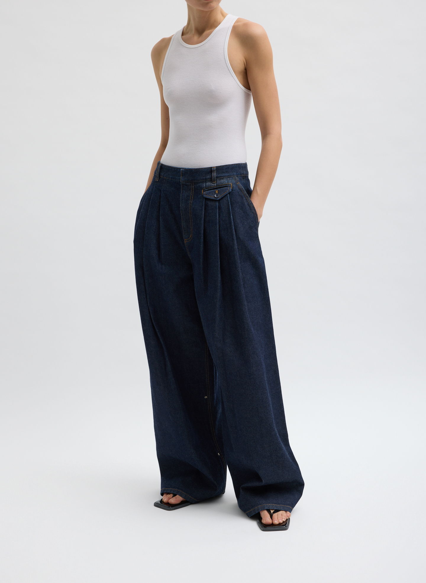Model wearing a white tank top and wide-leg dark jeans.