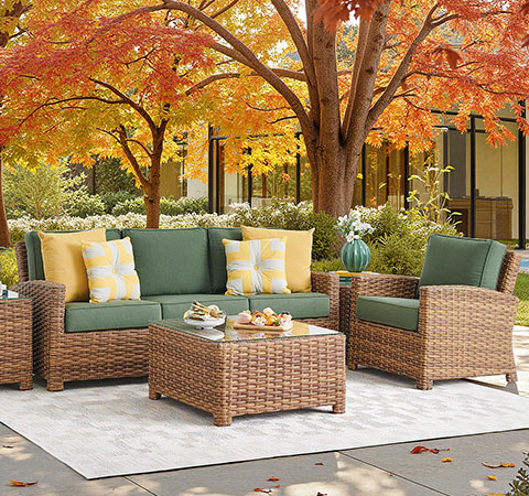 Outdoor seating area with green cushions, woven furniture, and autumn foliage.