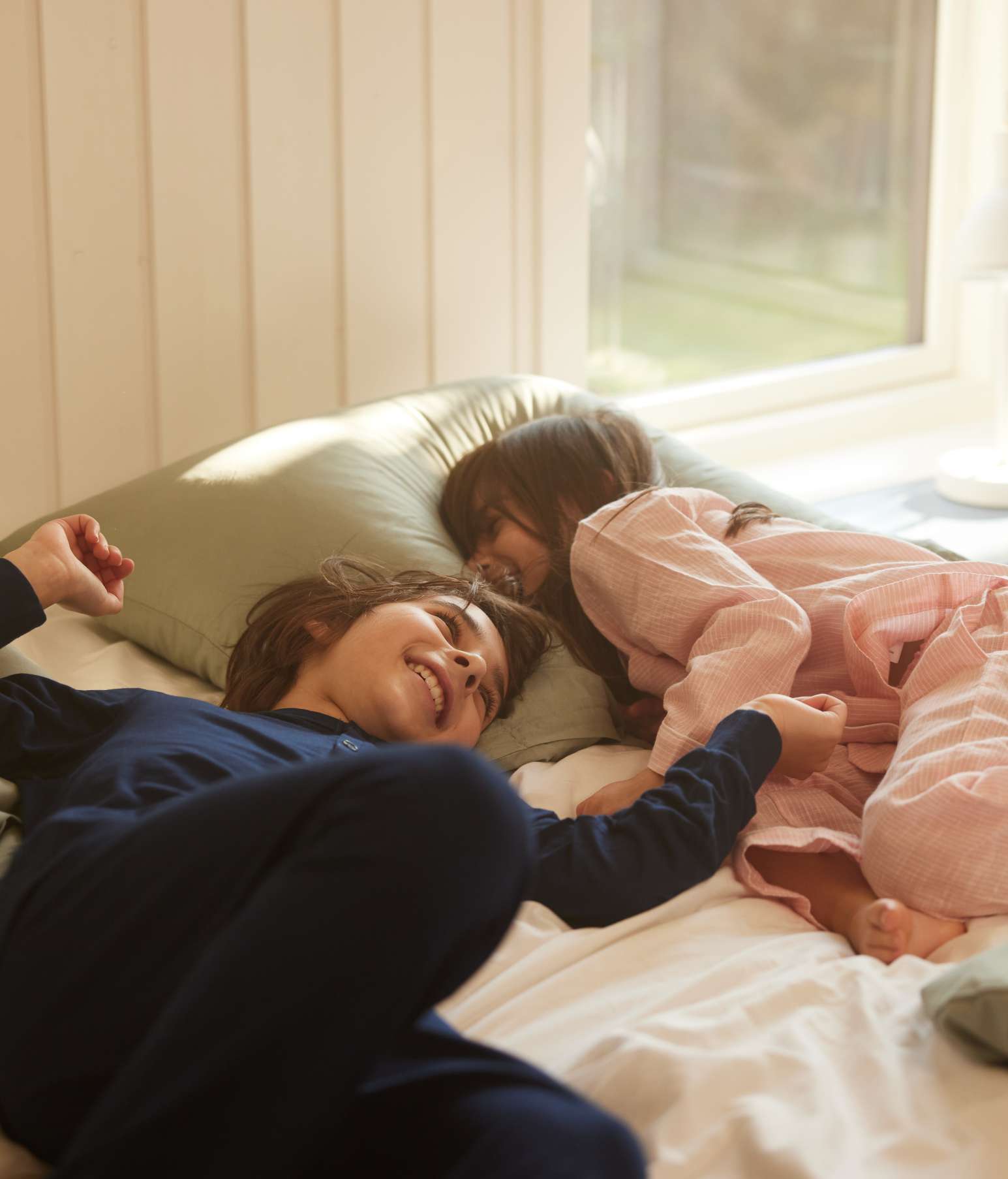 Brother and sister in pyjamas lying on the bed giggling – this is a dust mite hot spot so allergic kids may cough at night