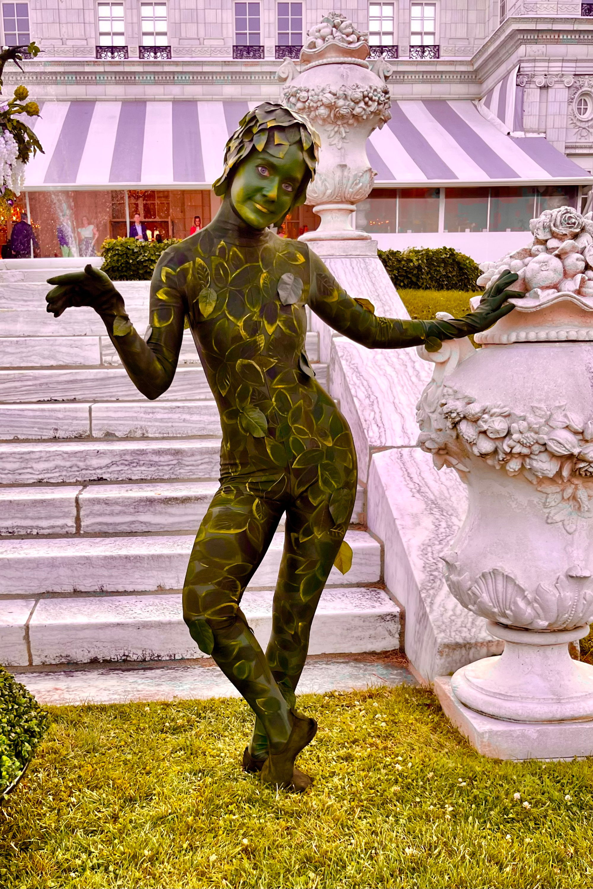 A green-painted performer posing in a garden setting at the Newport Flower Show in Rhode Island at the Breakers Mansion